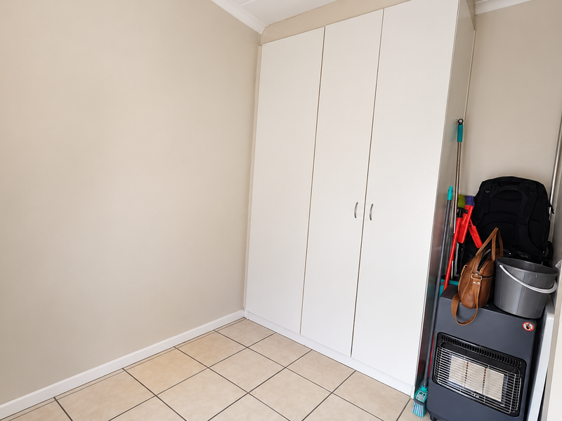 A clean, neutral bedroom featuring built-in cupboards and tiled flooring, offering a versatile space ready for personalization.