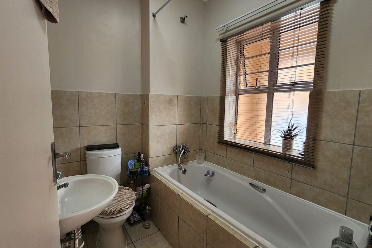 A functional bathroom featuring a bathtub with shower head, pedestal sink, toilet, and neutral wall and floor tiling.