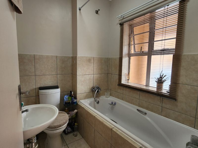 A functional bathroom featuring a bathtub with shower head, pedestal sink, toilet, and neutral wall and floor tiling.