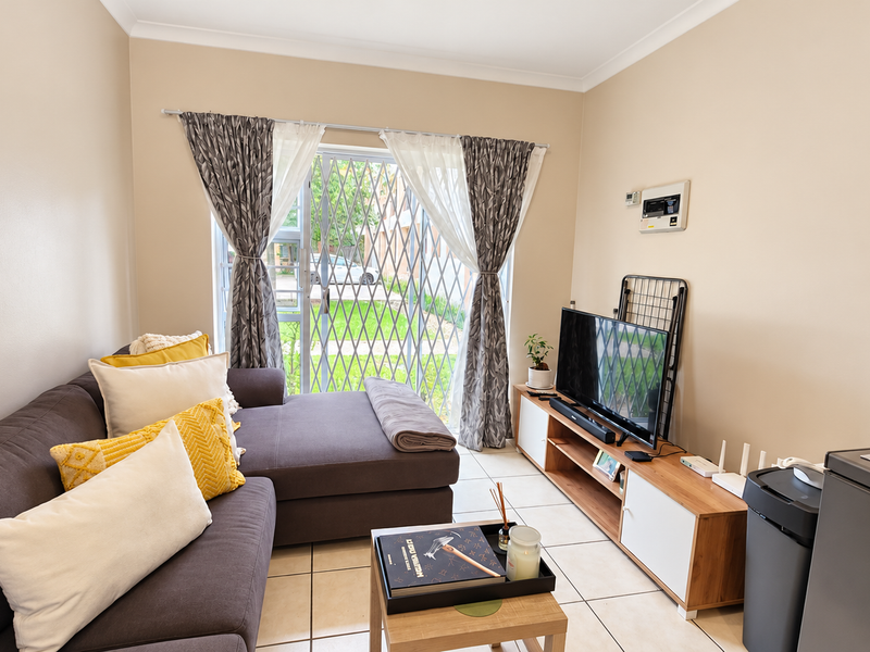 A comfortable living room featuring tiled flooring, neutral walls, and a sliding glass door with a security gate leading to the exterior.