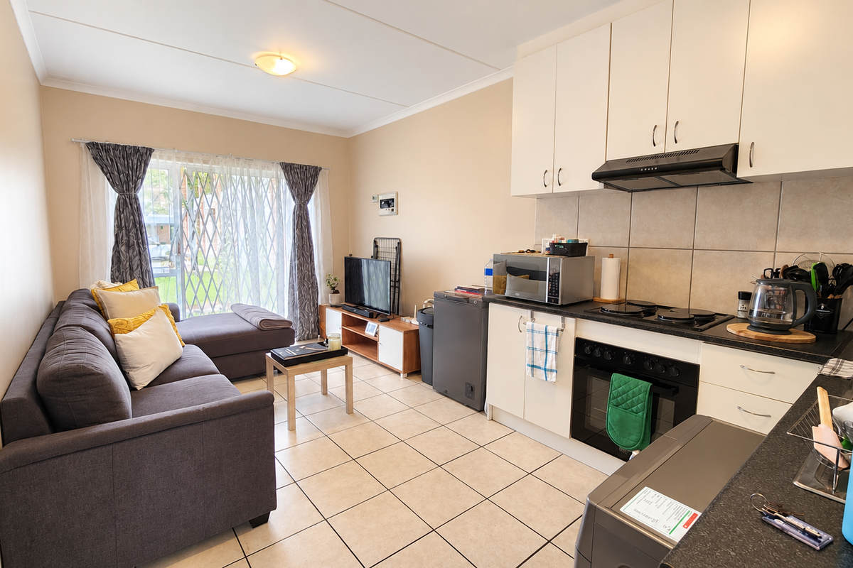 Open-plan living area featuring a functional kitchen with built-in cabinetry, electric hob, and oven, seamlessly flowing into a comfortable lounge with sliding door access.