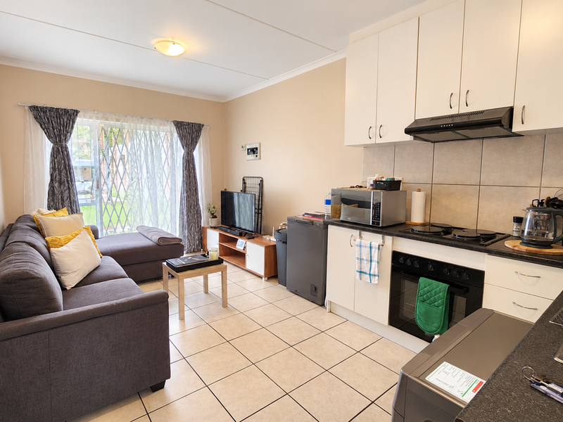 Open-plan living area featuring a functional kitchen with built-in cabinetry, electric hob, and oven, seamlessly flowing into a comfortable lounge with sliding door access.