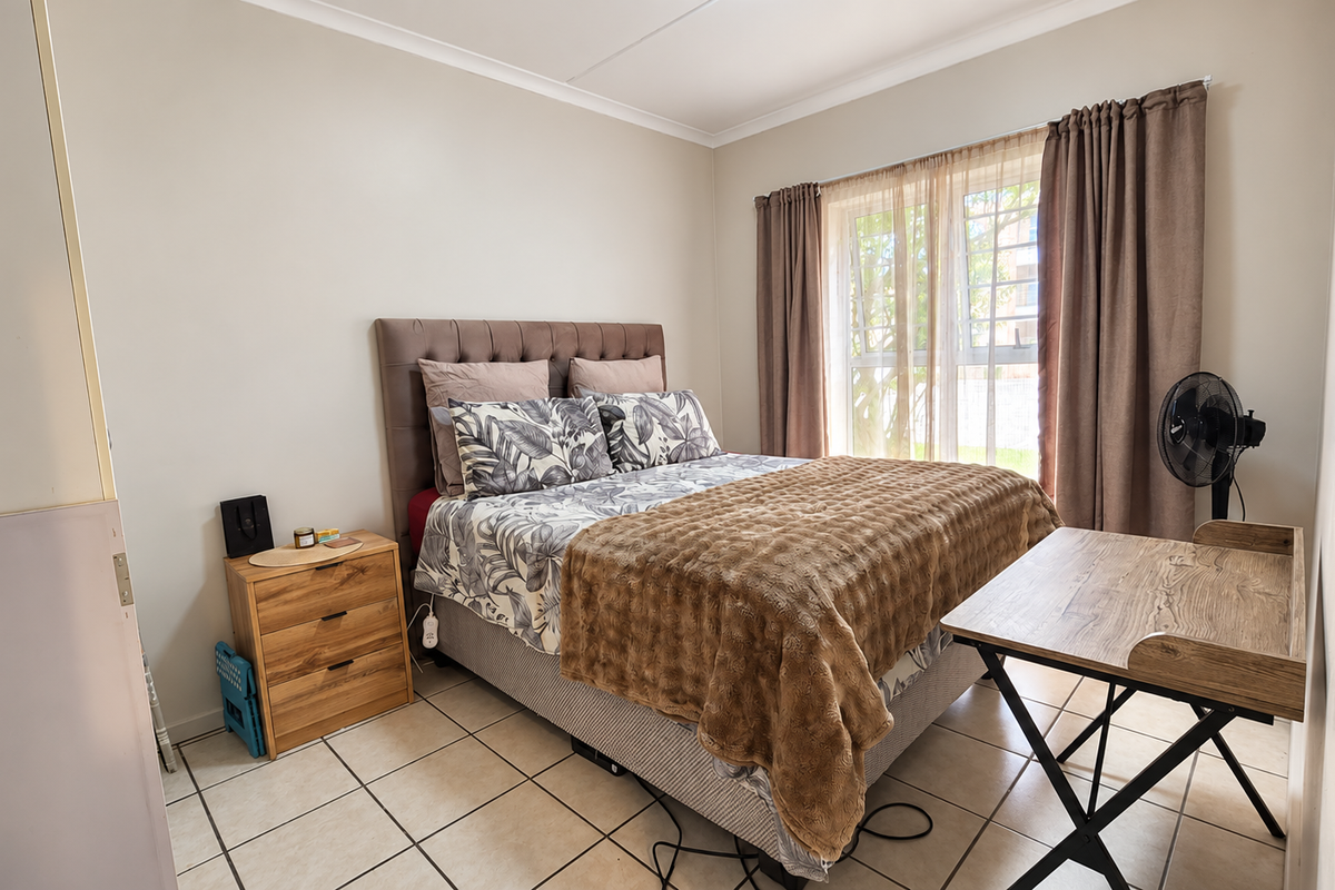 A functional bedroom featuring tiled flooring, a window with security bars, and neutral wall finishes, providing a comfortable and practical living space.
