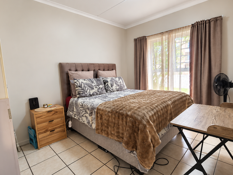 A functional bedroom featuring tiled flooring, a window with security bars, and neutral wall finishes, providing a comfortable and practical living space.