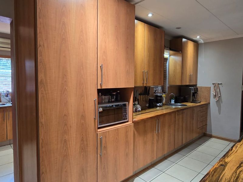 Spacious kitchen featuring wood veneer cabinetry, built-in microwave, gas hob, extractor fan, and tiled flooring with an adjacent laundry area.