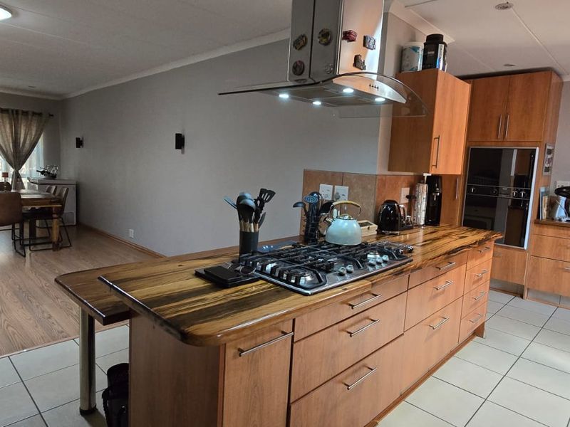 Spacious open-plan kitchen and dining area featuring a central island with gas hob, built-in oven, and warm-toned wooden cabinetry.
