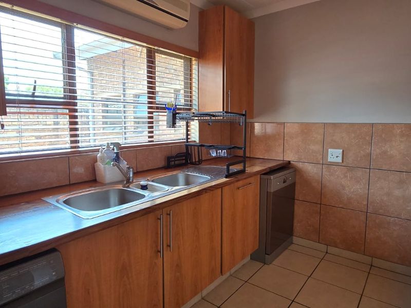 Functional scullery area featuring wood-look cabinetry, laminate countertops, a double stainless steel sink, and tiled splashbacks with integrated appliance space.