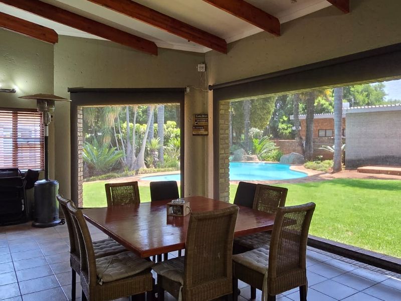 Spacious covered patio featuring exposed timber beams, tiled flooring, and a built-in bar, offering seamless indoor-outdoor flow to the garden and swimming pool area.