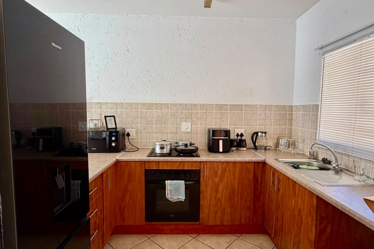 A functional U-shaped kitchen featuring wood-veneer cabinetry, laminate countertops, a built-in oven with hob, and a tiled backsplash.