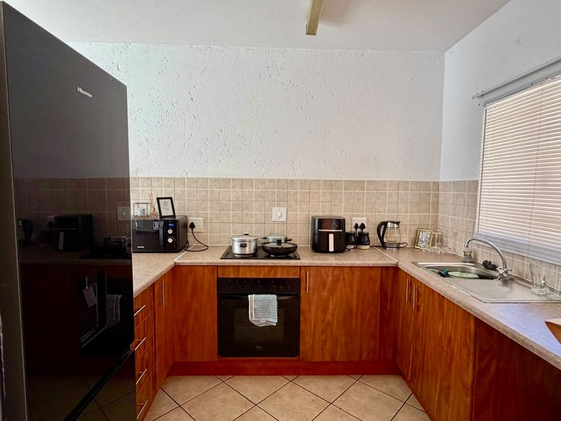 A functional U-shaped kitchen featuring wood-veneer cabinetry, laminate countertops, a built-in oven with hob, and a tiled backsplash.