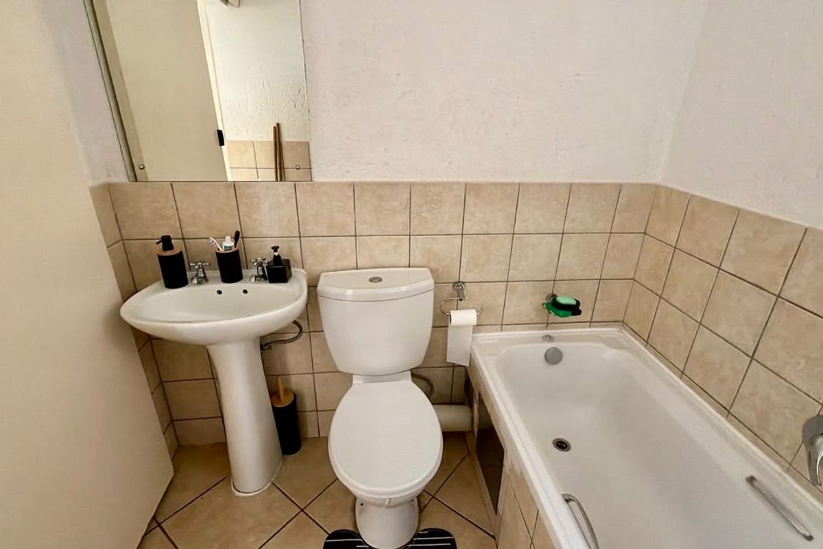 A functional bathroom featuring a pedestal basin, standard toilet, and a bathtub with neutral wall and floor tiling.