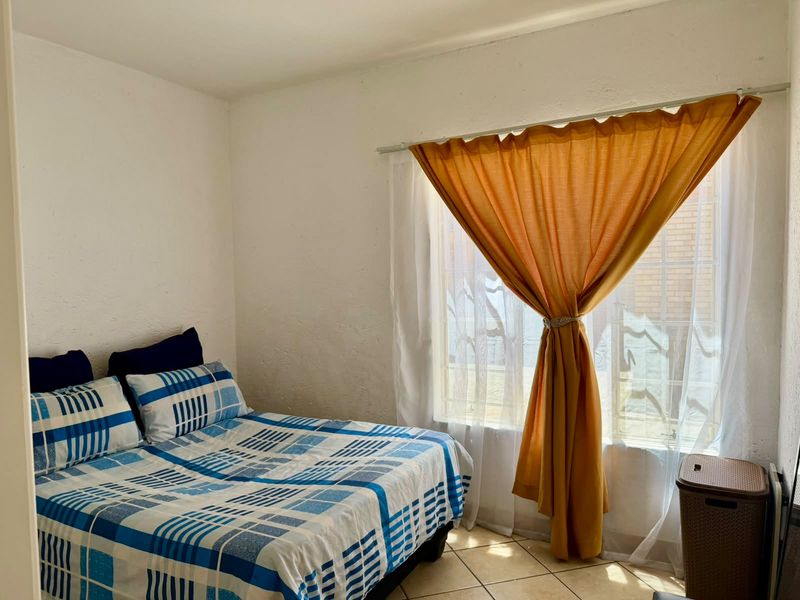 A simple bedroom featuring tiled flooring and a window fitted with security bars, providing natural light.