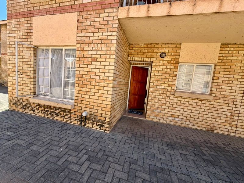 Exterior view of an apartment entrance featuring face brick construction, a paved walkway, and a timber front door with aluminium window frames.