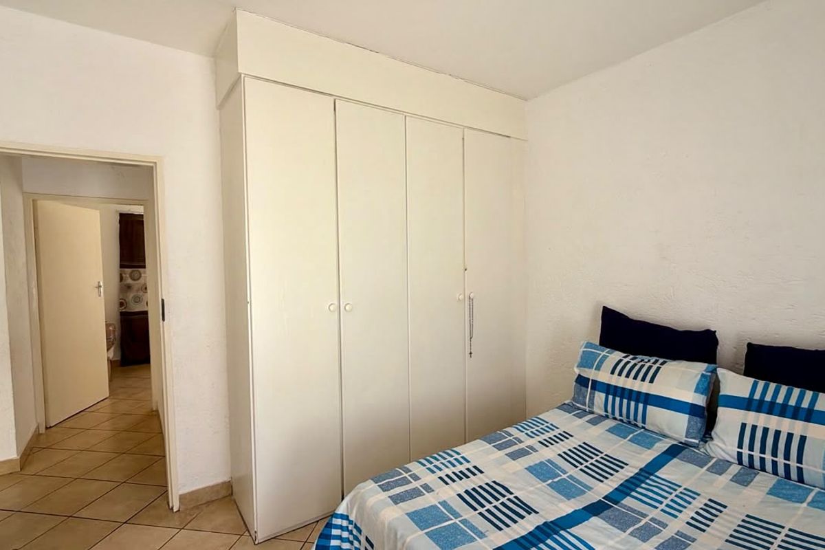 A bedroom featuring a white built-in wardrobe and tiled flooring, providing functional storage space within the room.
