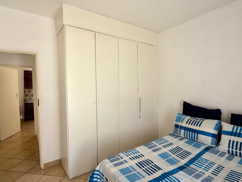 A bedroom featuring a white built-in wardrobe and tiled flooring, providing functional storage space within the room.