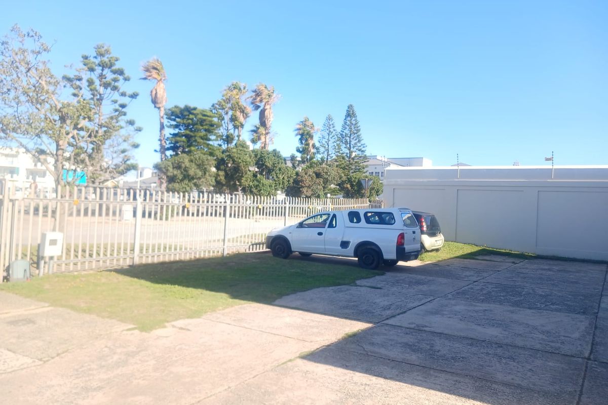 Rear exterior area featuring a paved driveway, perimeter fencing with electric security, and a boundary wall.