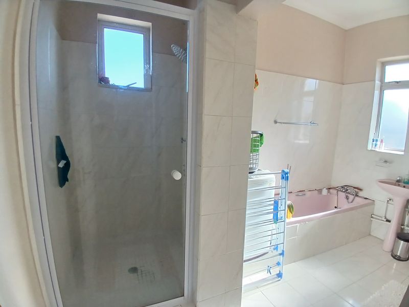 A functional bathroom featuring a separate shower enclosure, a built-in bathtub, and a pedestal sink with tiled finishes throughout.