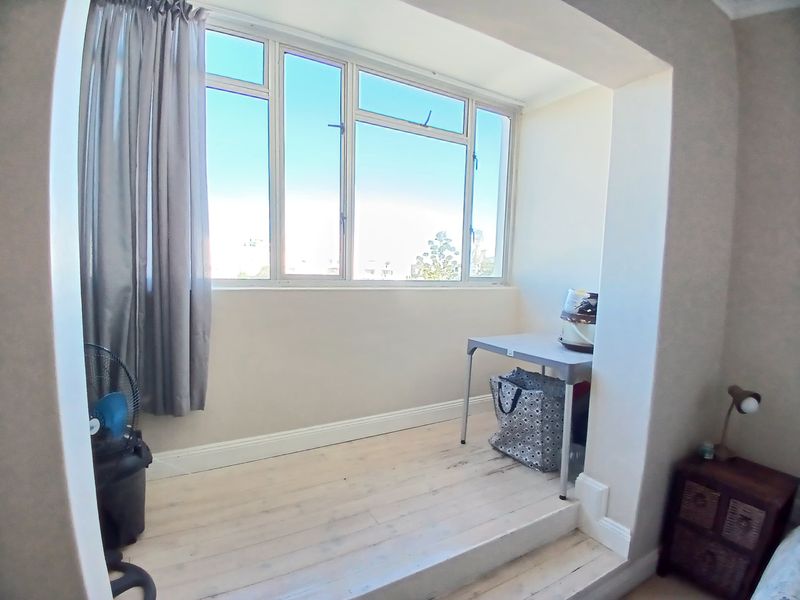 A bedroom featuring a raised platform area with large windows, providing natural light and a view, finished with light-toned timber flooring.