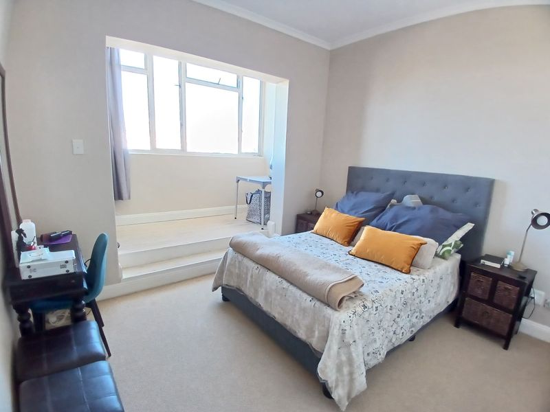 A spacious bedroom featuring a unique raised sunroom area with large windows, providing ample natural light and a versatile space for a study or seating.