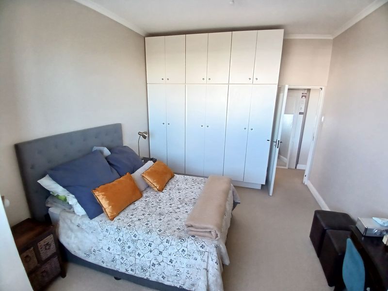 A well-maintained bedroom featuring neutral walls, carpeted flooring, and extensive floor-to-ceiling built-in cupboards providing ample storage space.