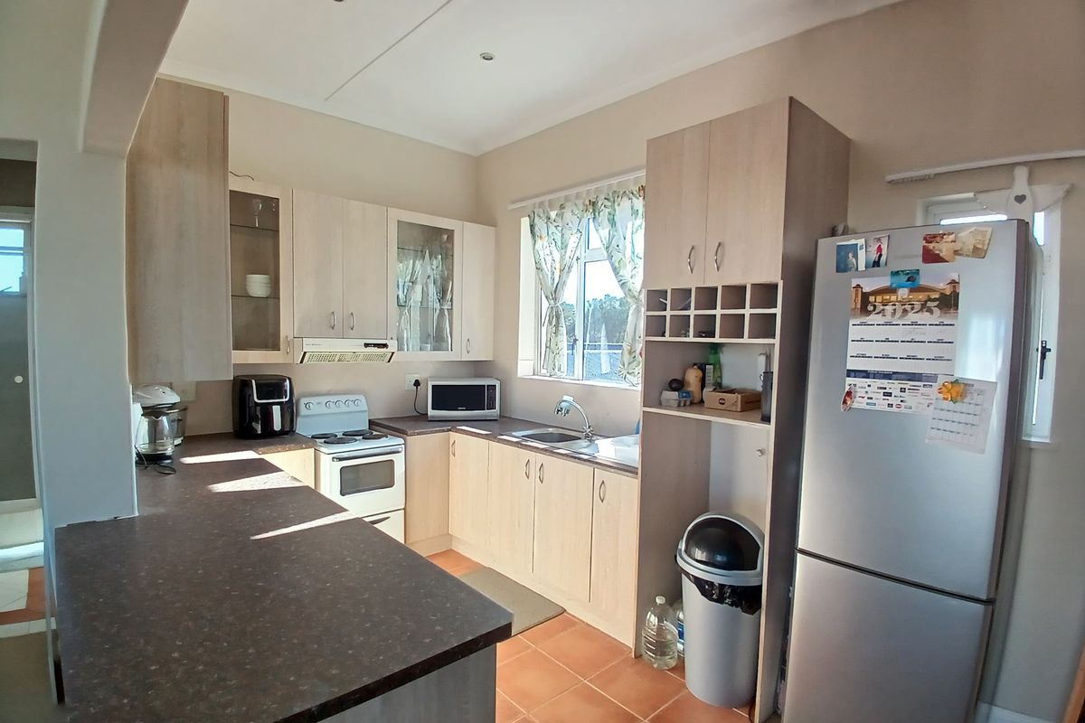 Functional kitchen featuring light wood-tone cabinetry, dark laminate countertops, a stainless steel sink, and a freestanding stove with an integrated extractor fan.