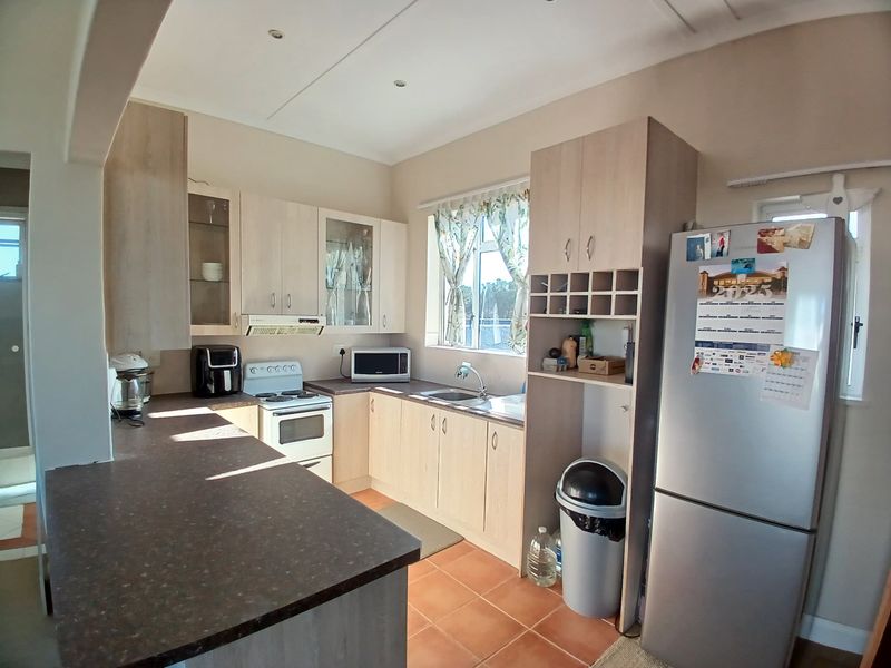 Functional kitchen featuring light wood-tone cabinetry, dark laminate countertops, a stainless steel sink, and a freestanding stove with an integrated extractor fan.