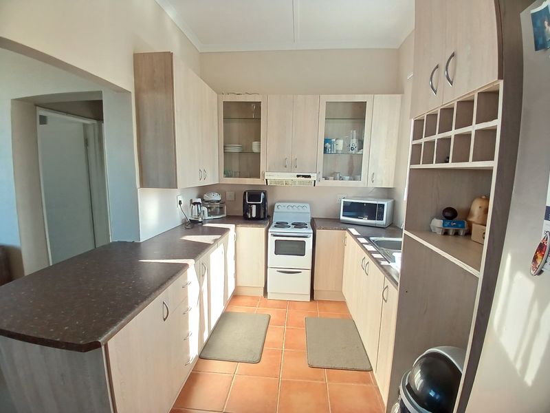 A functional kitchen featuring light wood-tone cabinetry, dark laminate countertops, a freestanding stove with extractor, and tiled flooring with a built-in wine rack.