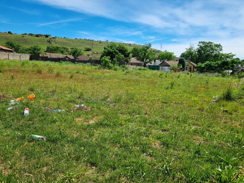 A vacant residential plot featuring open grassed land with perimeter boundary walls and surrounding neighborhood views.