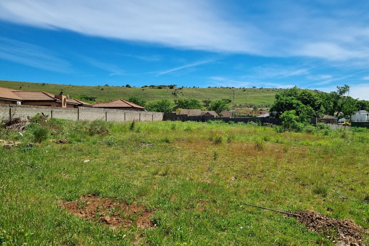 A vacant residential plot featuring natural grass coverage and a perimeter boundary wall, set against a scenic hillside backdrop.