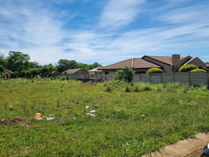 A vacant residential plot featuring a precast concrete boundary wall and overgrown grass, situated in a suburban neighborhood.