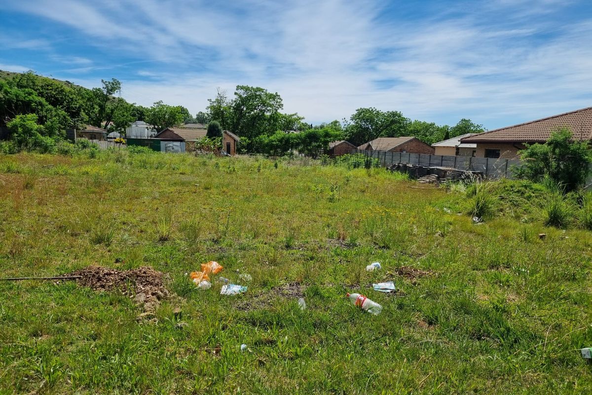 A vacant residential plot featuring overgrown grass and a precast concrete boundary wall, situated in a suburban neighborhood setting.