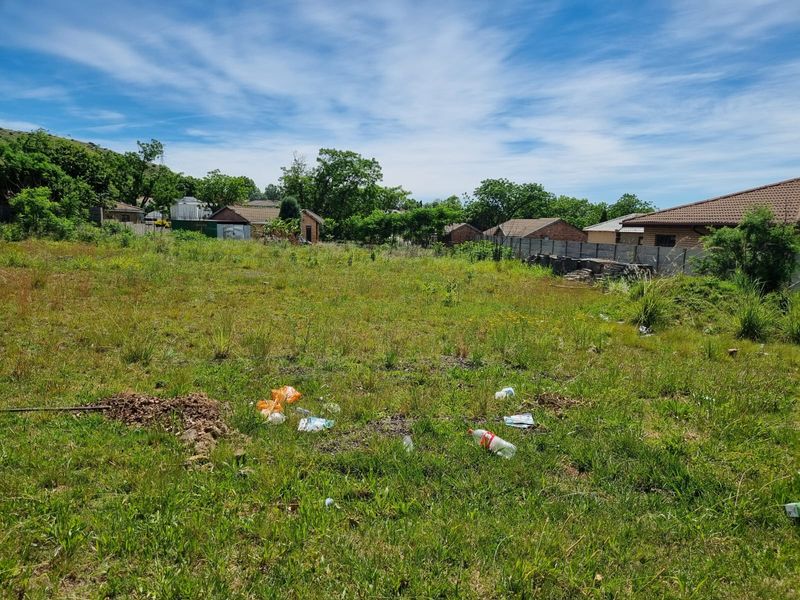 A vacant residential plot featuring overgrown grass and a precast concrete boundary wall, situated in a suburban neighborhood setting.