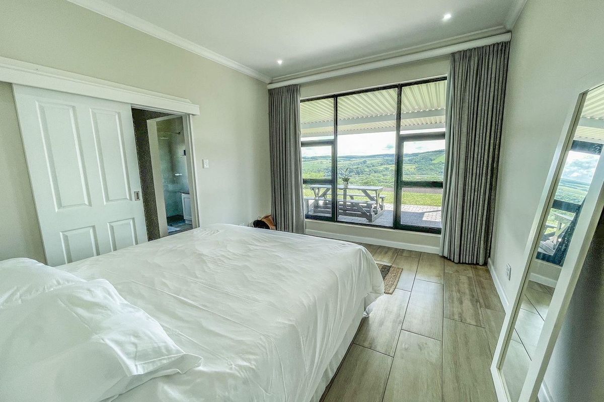 A bright bedroom featuring wood-look tile flooring, recessed lighting, and a large window with sliding door access to a patio offering scenic landscape views.