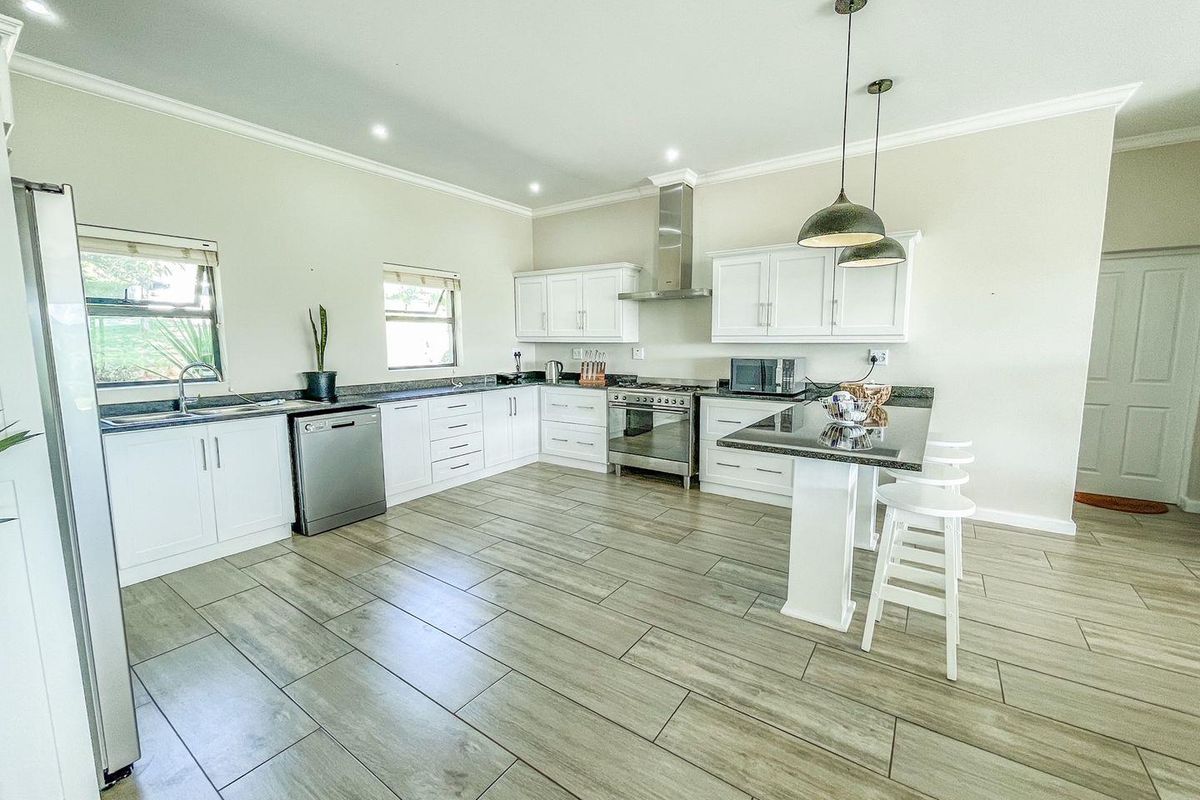 Modern kitchen featuring white cabinetry, granite countertops, a central island, stainless steel appliances, and wood-look tile flooring.
