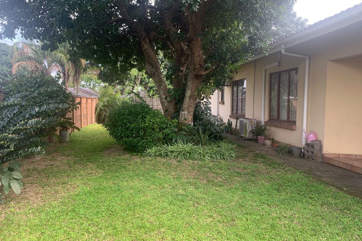 A view of the rear garden featuring a large mature tree, lawn area, and paved walkway along the side of the house.
