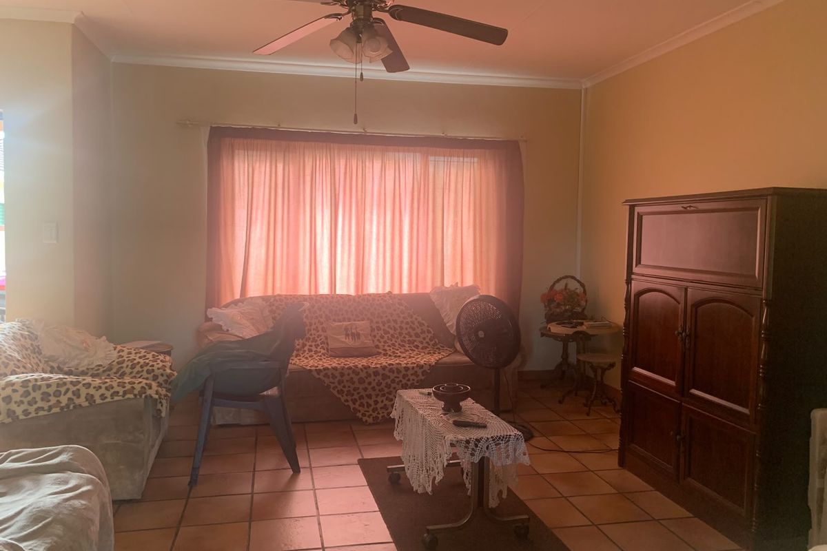 A living room featuring terracotta floor tiles, a ceiling fan, and coved ceilings, offering a dated but functional space ready for modernization.