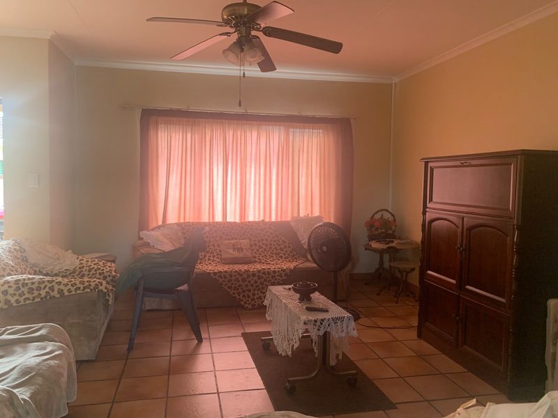 A living room featuring terracotta floor tiles, a ceiling fan, and coved ceilings, offering a dated but functional space ready for modernization.