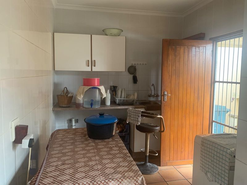 A functional scullery area featuring tiled walls, built-in cabinetry, a sink, and direct access to the exterior via a timber door.