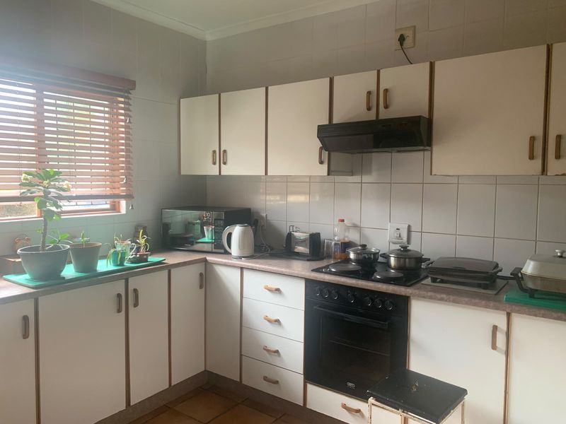 A functional kitchen featuring white built-in cabinetry, laminate countertops, a tiled backsplash, and integrated cooking appliances, offering a classic layout with potential for modernization.