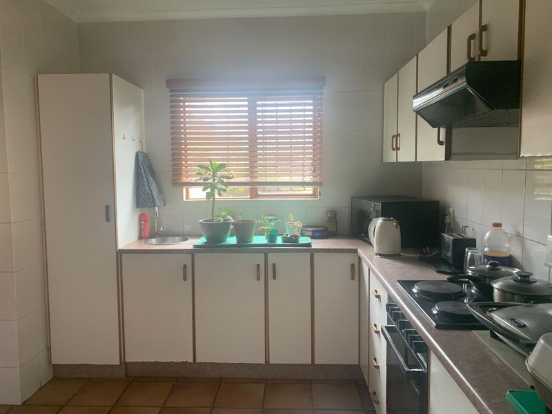 A functional kitchen featuring white built-in cabinetry, laminate countertops, tiled splashbacks, and integrated cooking appliances including an oven and hob.