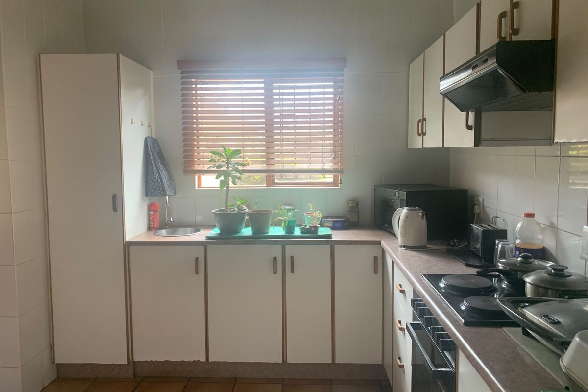 A functional kitchen featuring white built-in cabinetry, laminate countertops, tiled splashbacks, and integrated cooking appliances including an oven and hob.