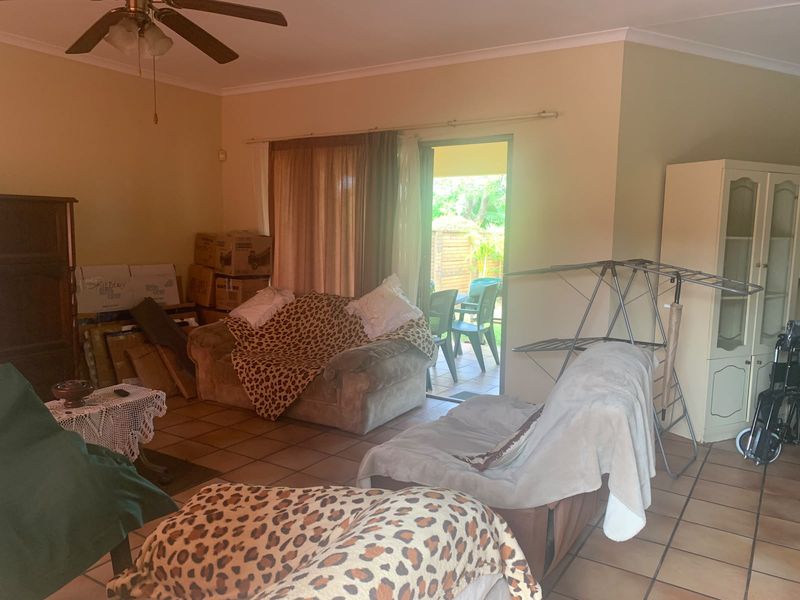 A living room featuring tiled flooring, a ceiling fan, and a sliding glass door providing access to the outdoor patio area.