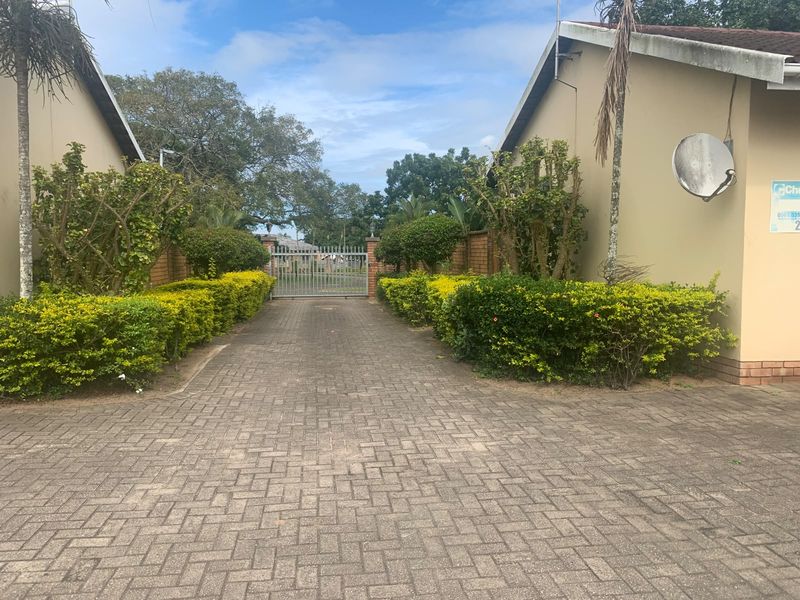 A paved driveway leading to a secure metal gate, flanked by established hedges and residential building facades.
