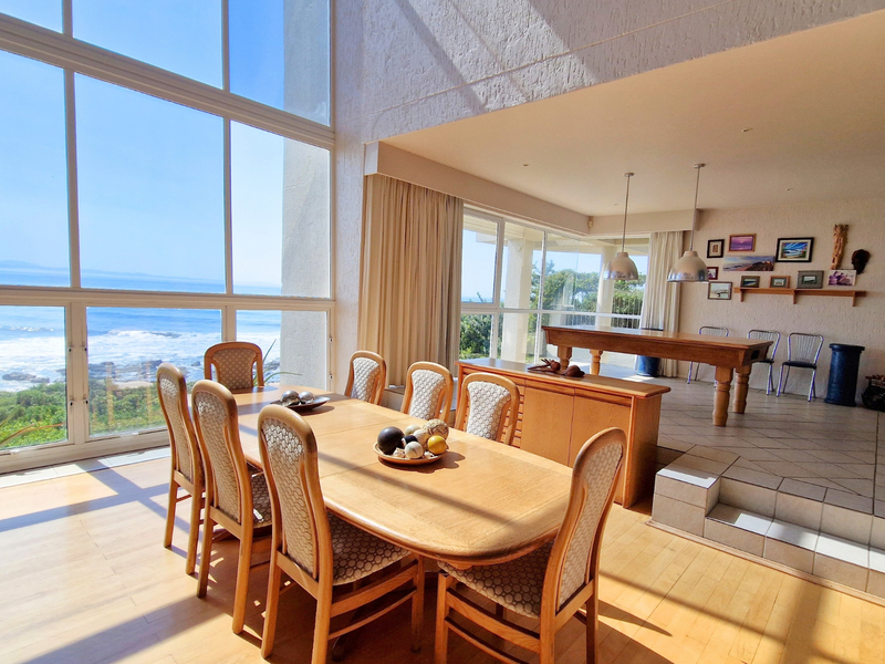 Spacious open-plan living and dining area featuring floor-to-ceiling windows with panoramic ocean views, a sunken lounge, and a built-in fireplace.