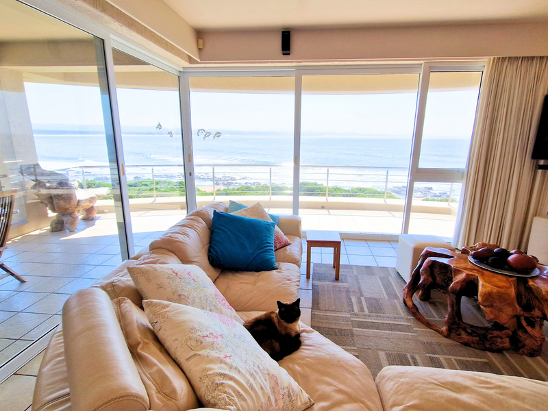 Spacious living room featuring large sliding glass doors that open onto a balcony with expansive ocean views and tiled flooring throughout.