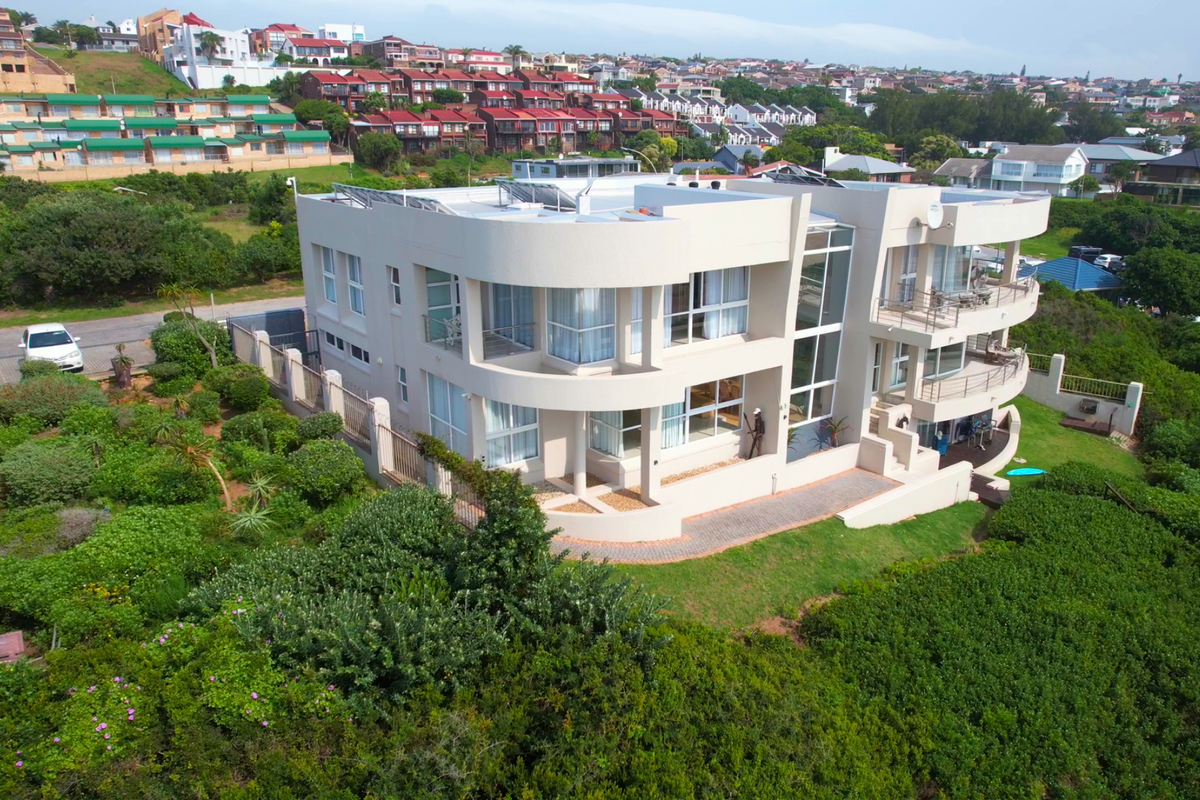 Aerial view of a modern multi-level residential property featuring curved balconies, large glass windows, and solar panels, set within a landscaped coastal environment.