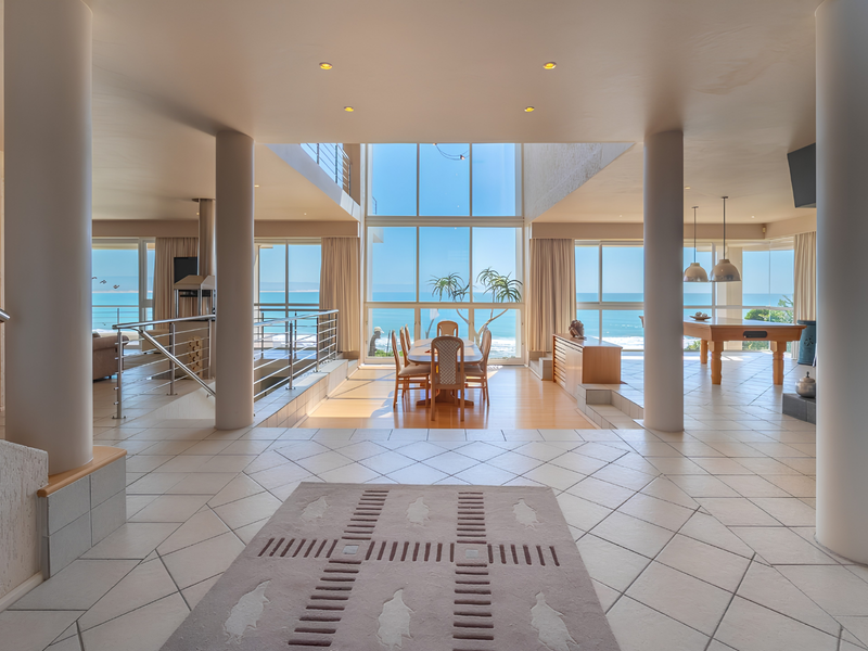 Spacious open-plan living area featuring floor-to-ceiling windows with panoramic ocean views, tiled flooring, and a prominent central staircase with modern balustrades.
