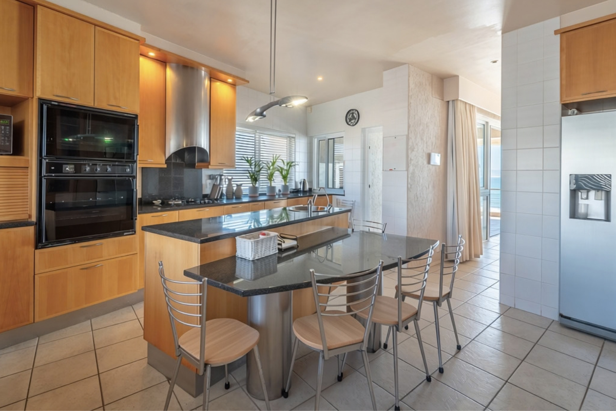 A functional kitchen featuring light wood cabinetry, granite countertops, a central island with integrated seating, and built-in appliances, with tiled flooring throughout.