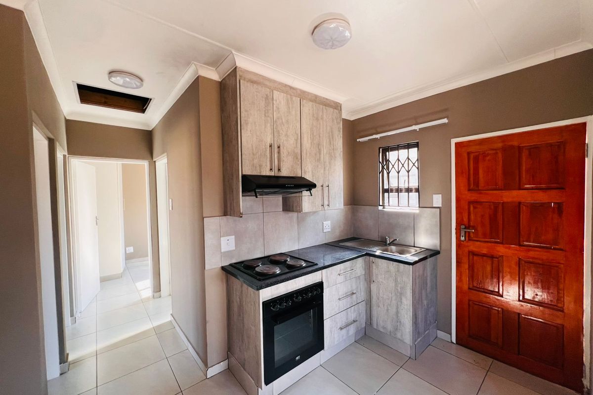 Compact kitchen featuring modern wood-look cabinetry, built-in oven and hob, tiled flooring, and direct access to the interior hallway.