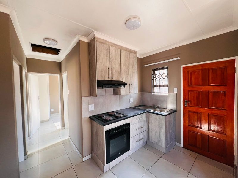 Compact kitchen featuring modern wood-look cabinetry, built-in oven and hob, tiled flooring, and direct access to the interior hallway.